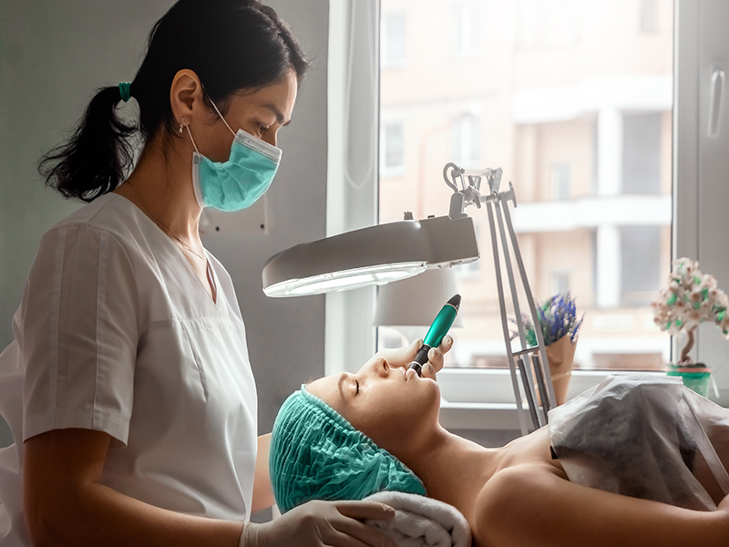A beautician wearing medical gloves cleans the pores on the face using special equipment while looking through a magnifying glass. The concept of facial hygiene, cosmetic procedures, skin care
